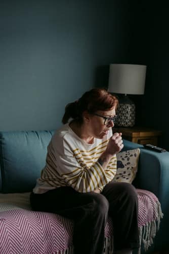 Woman sitting on couch coughing.