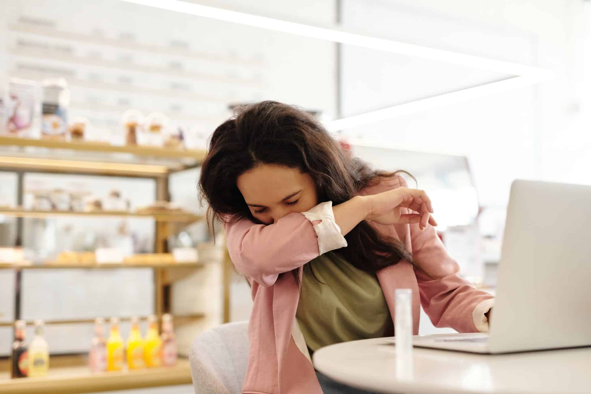 Woman sneezing into her elbow while at a cafe.