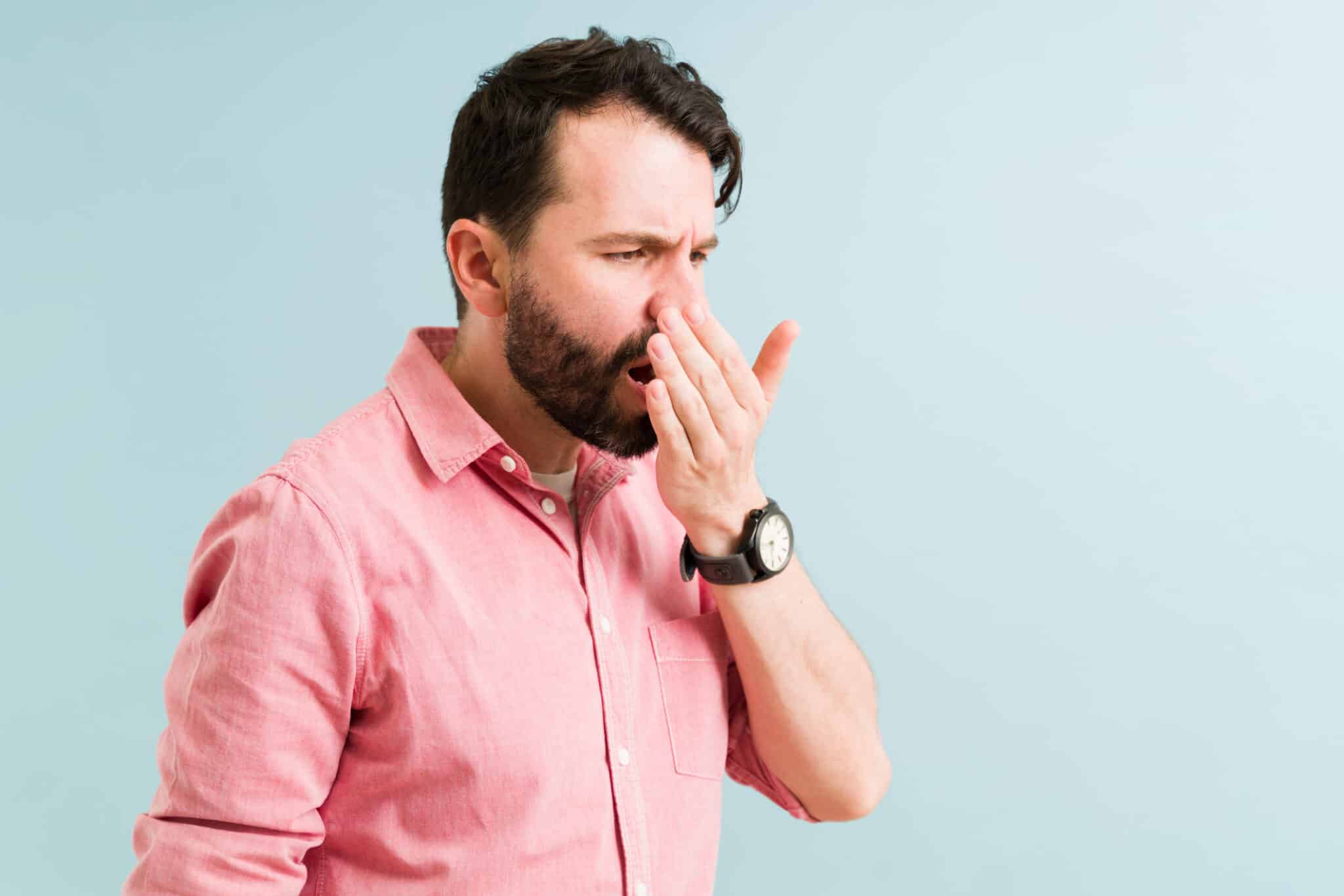 Younger man holding his hand up to his mouth to check his breath.